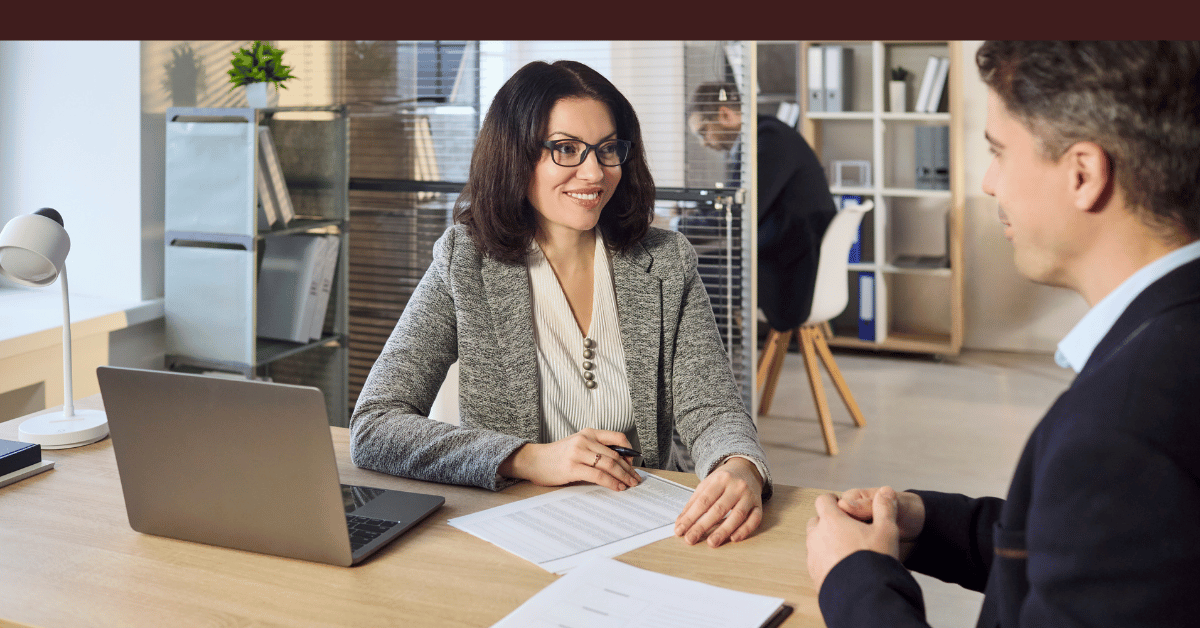 Professional woman consulting with a client at a desk with a laptop and paperwork.